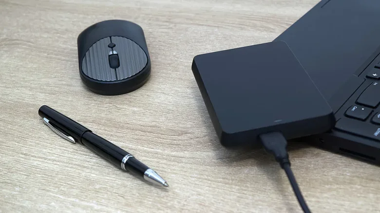 An external HDD on a laptop, next to a pen and mouse.