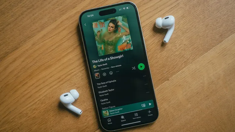 An iPhone with two AirPods showing Taylor Swift's "The Life of a Showgirl" album on Spotify.