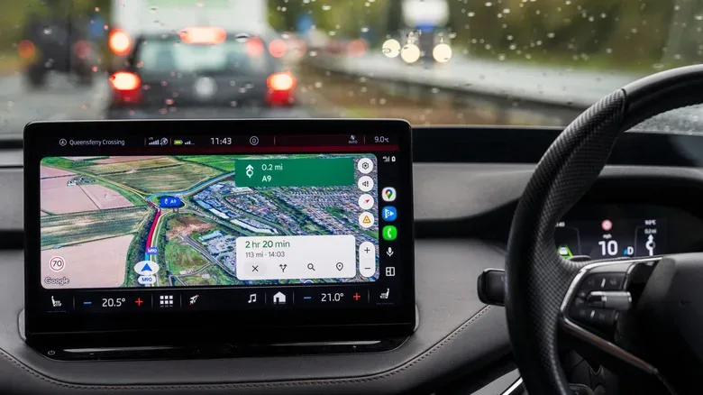 An in-car infotainment display shows a Google Maps navigation route while the vehicle is being driven in rainy traffic.