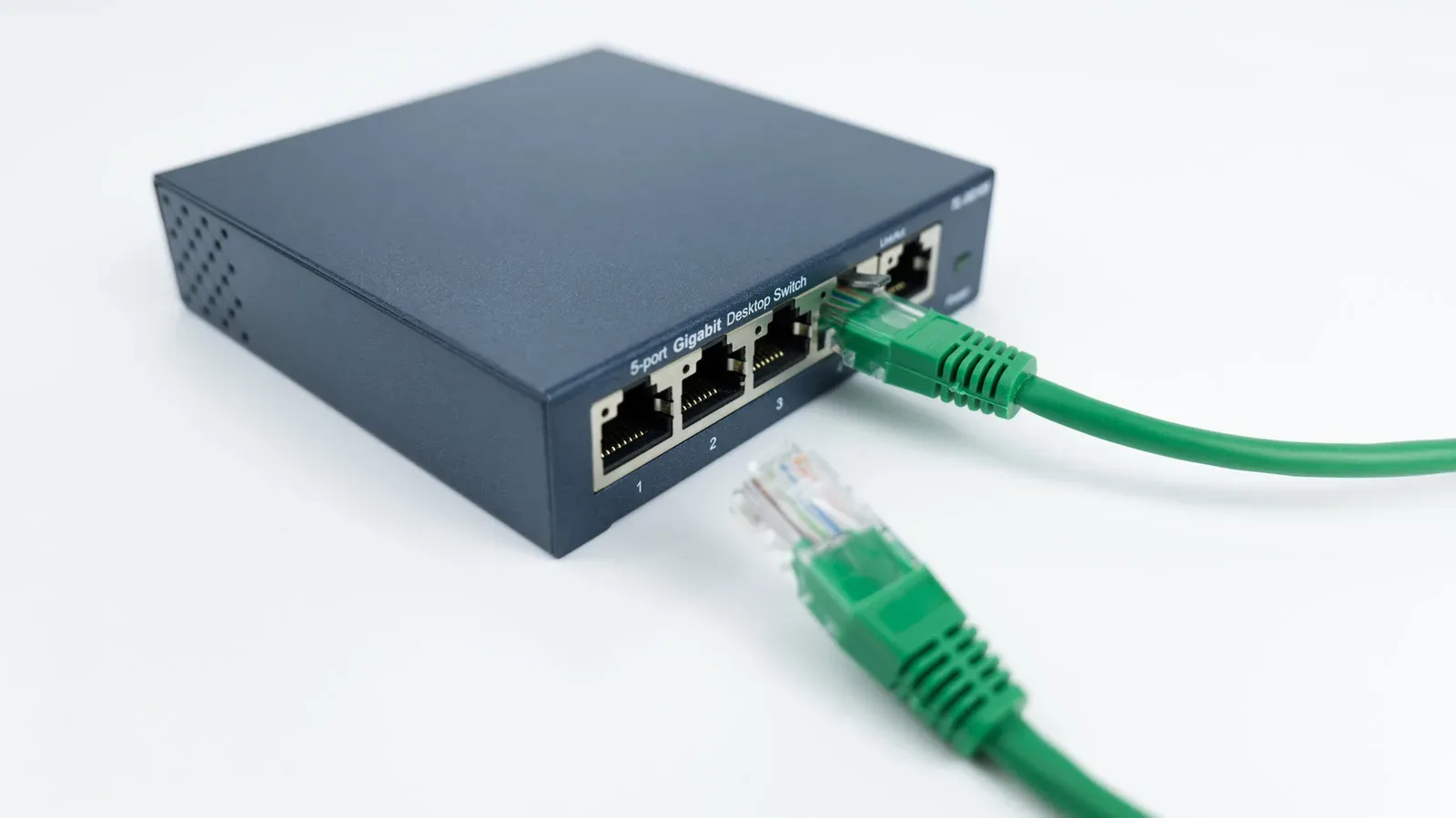A compact Ethernet switch connected to a home router beside a game console and gaming PC