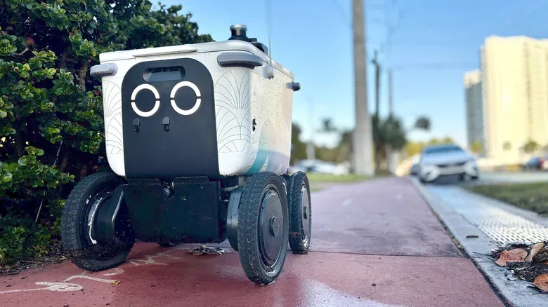 Delivery robot paused near a sidewalk curb and pedestrian crossing