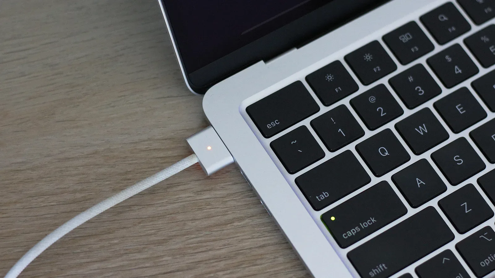 A MacBook connected to a magnetic MagSafe charging cable on a desk
