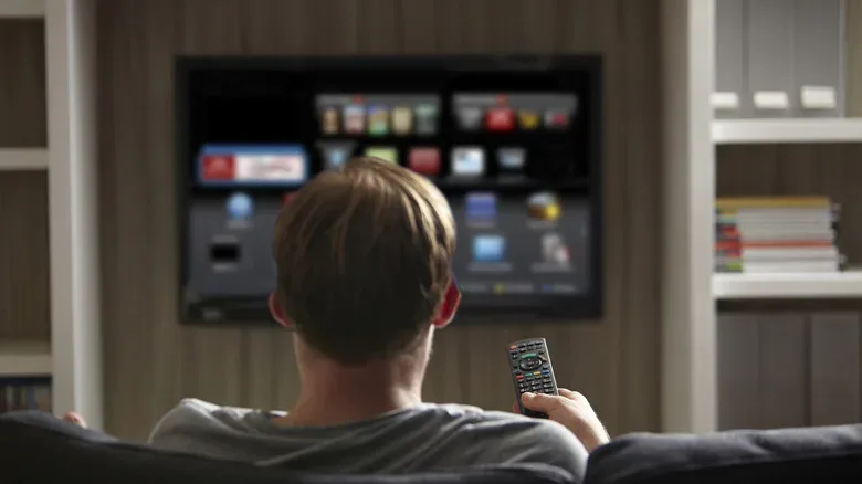 A man holding a TV remote, pointing it towards a smart TV.