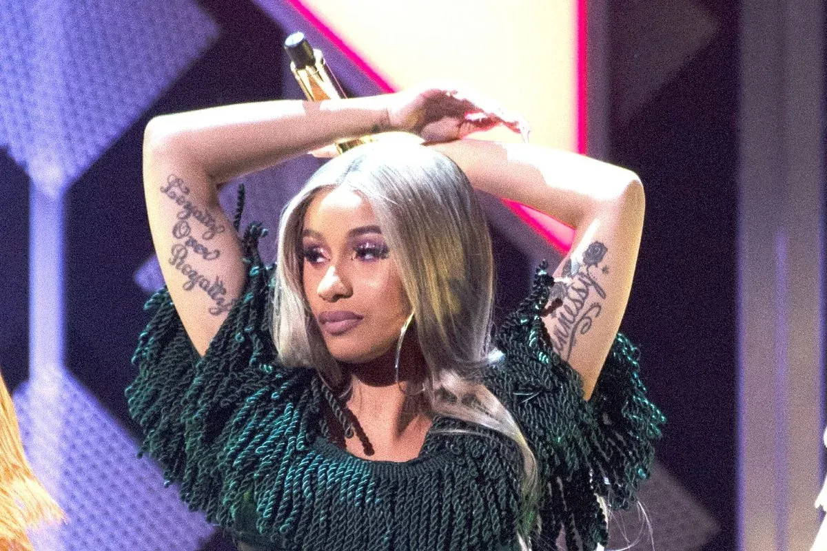 Cardi B wearing a white open-back catsuit while displaying a diamond piercing