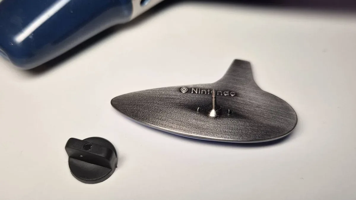 Photo of the back of the Ocarina of Time pin sitting on a white desk.