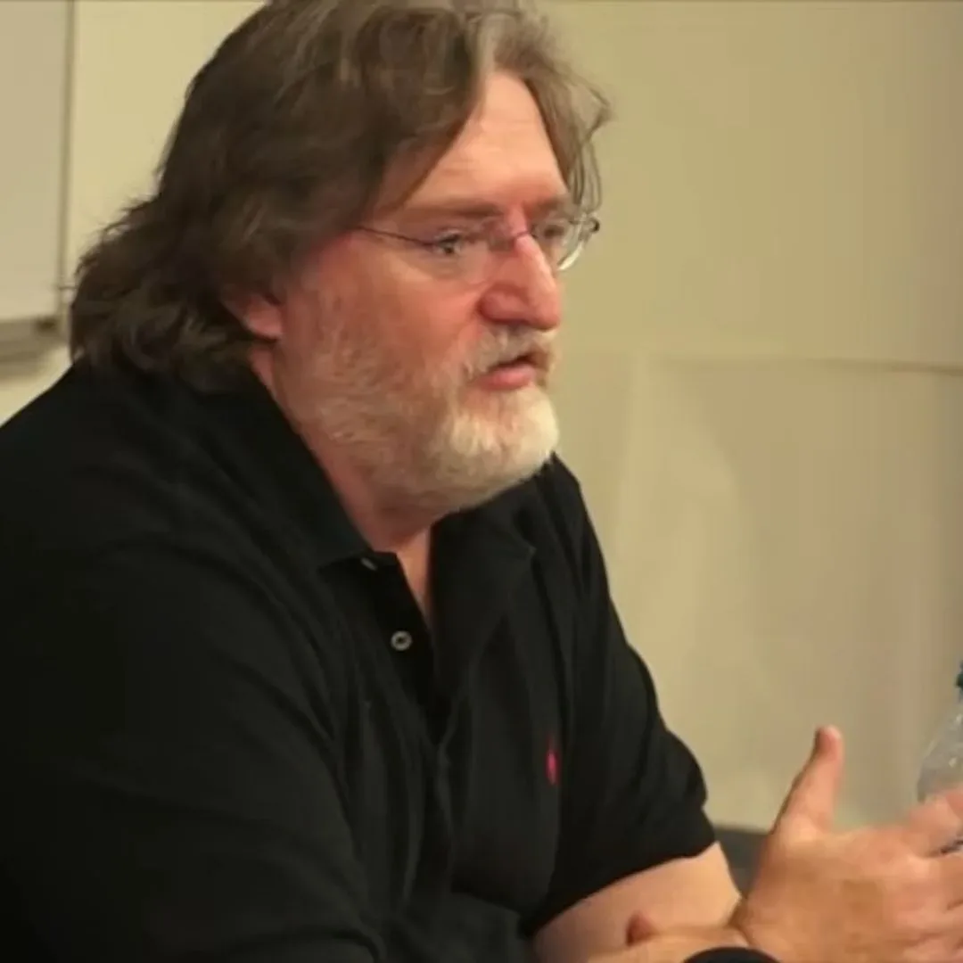 Gabe Newell in black shirt sitting at white desk for 2013 university talk
