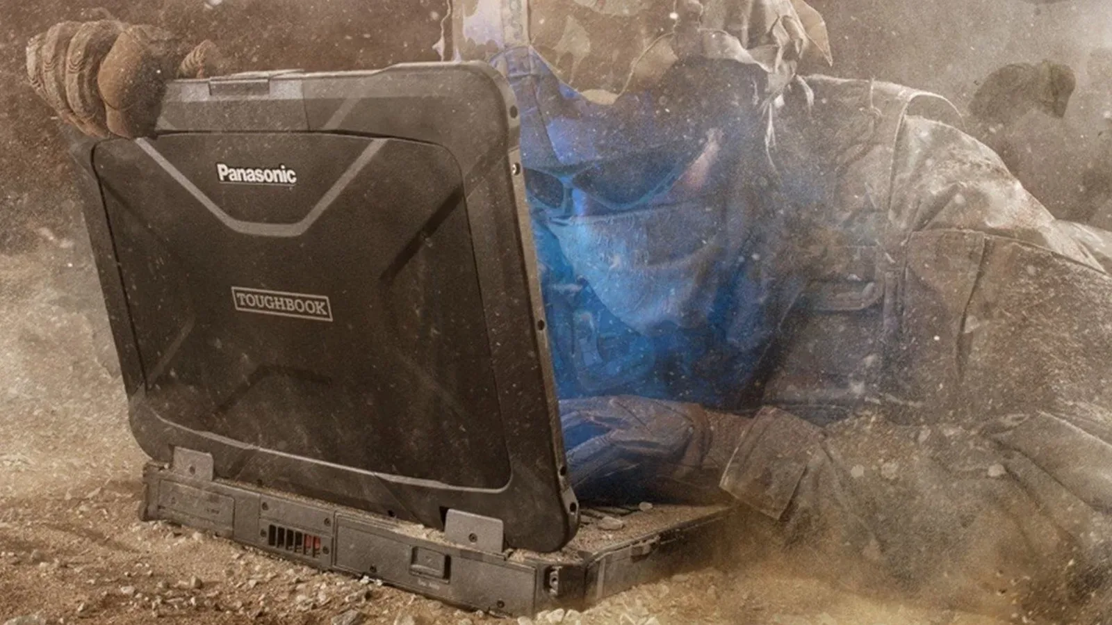 A rugged laptop with reinforced corners and covered ports on an outdoor work surface