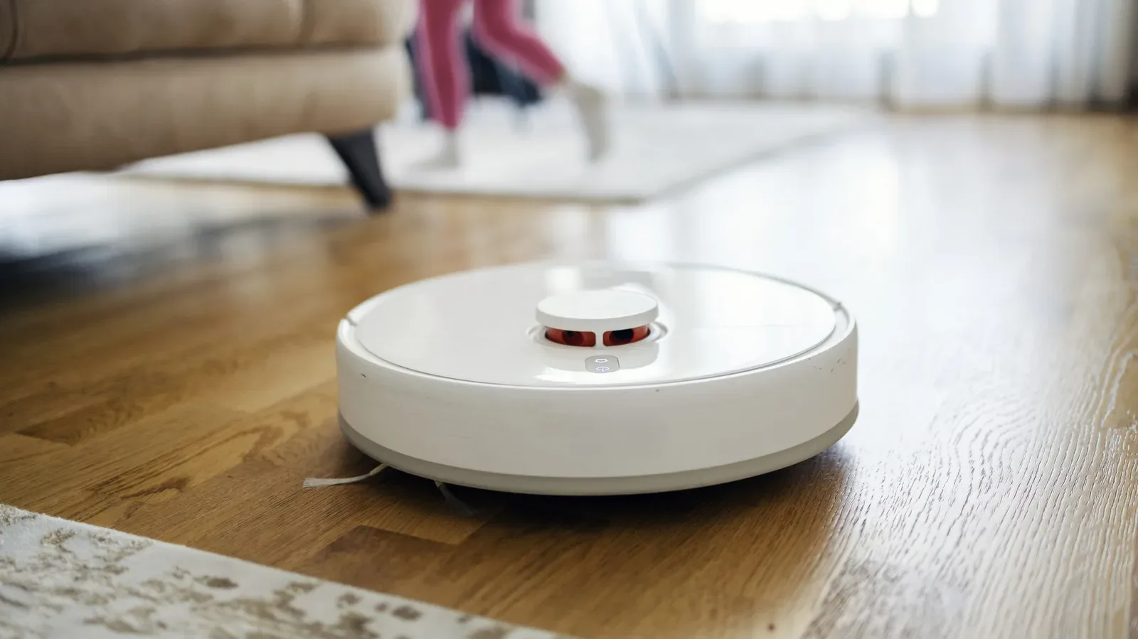 A circular robot vacuum navigating around a charging cable on a hard floor