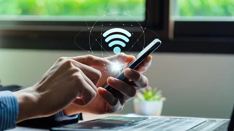 Person using a smartphone beside a laptop with a Wi-Fi connection symbol overlay.