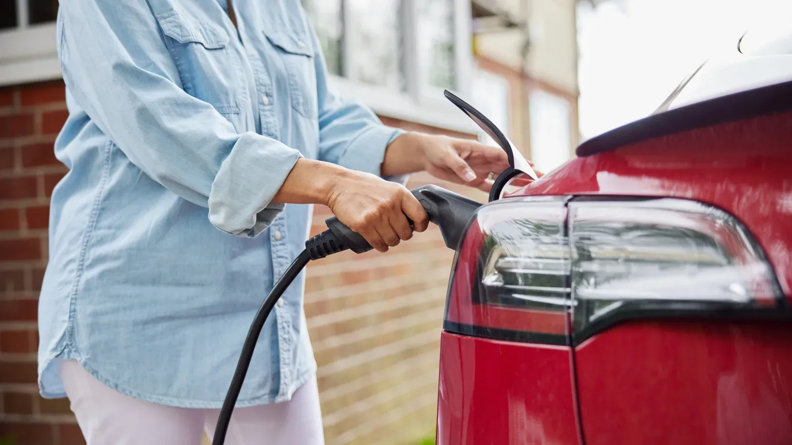 An electric vehicle charging at a home outlet beside a garage