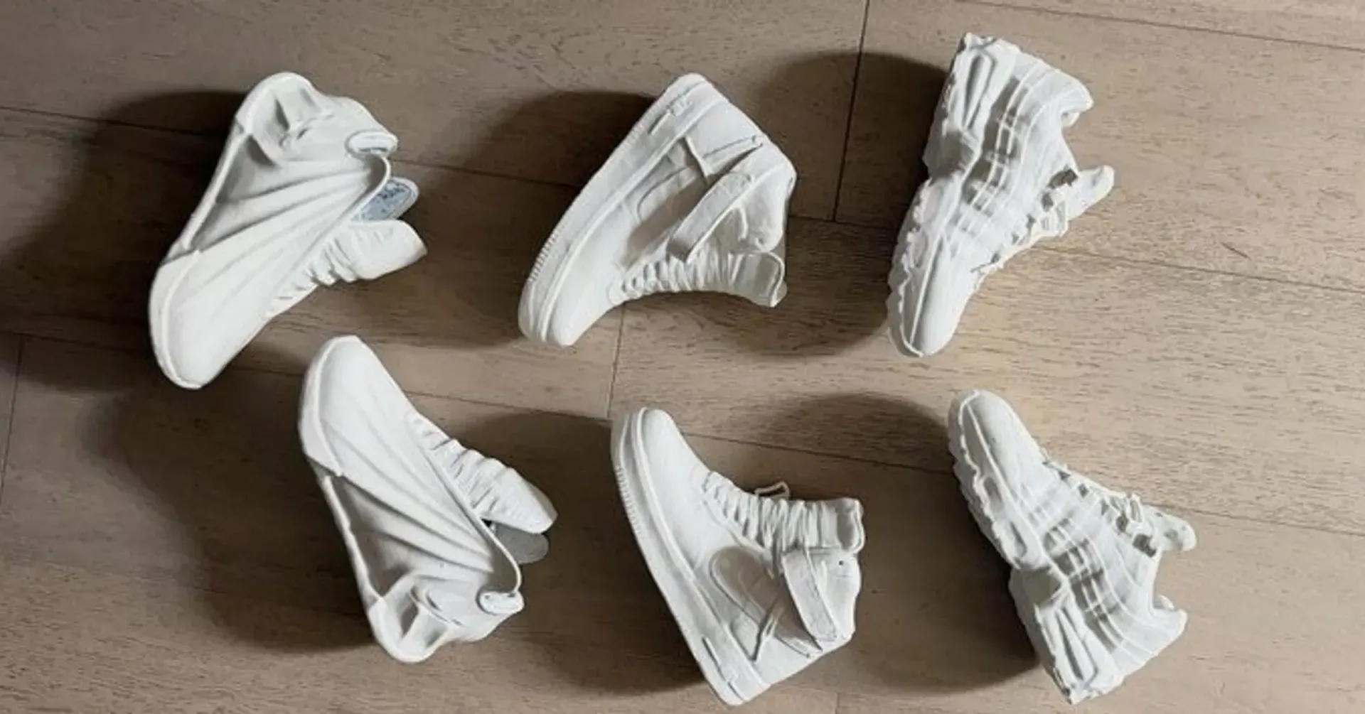 Sculptural white Nike shoe forms resembling the Air Max 95, Air Force 1 and GT Future arranged on a wood floor