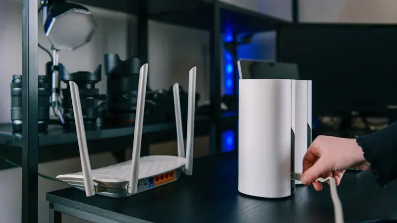 Person connecting an Ethernet cable to a mesh Wi-Fi node beside a traditional wireless router.