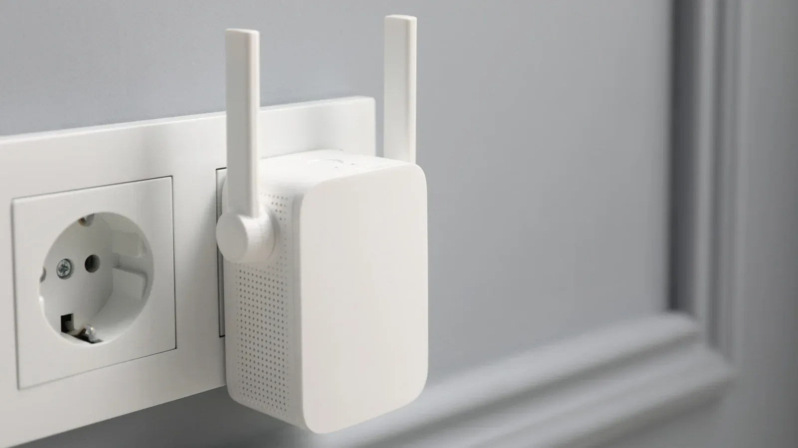 A Wi-Fi extender plugged into a hallway outlet between a router and adjacent rooms