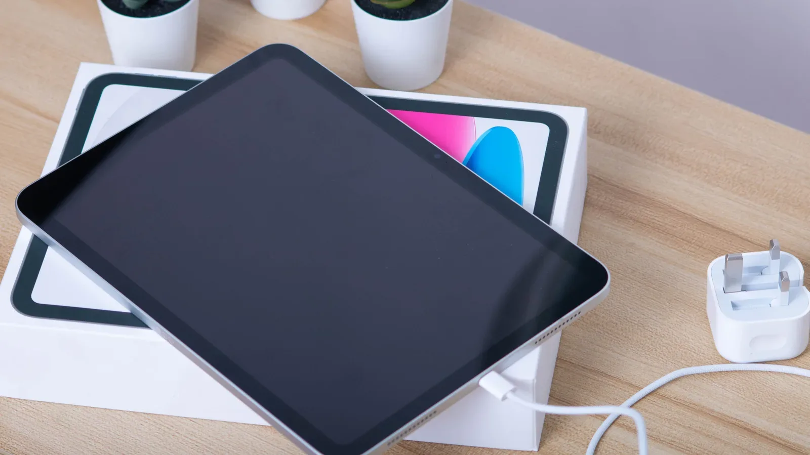 An iPad connected to a charging cable beside a wall adapter