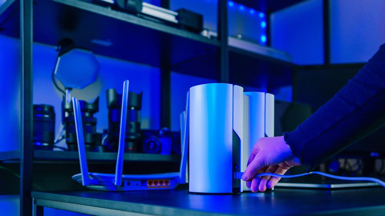 A minimalist mesh Wi-Fi node on a shelf beside a gaming setup