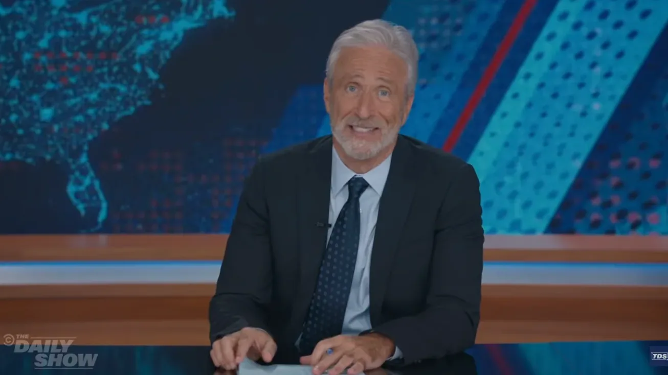 Jon Stewart behind The Daily Show desk during a political comedy monologue