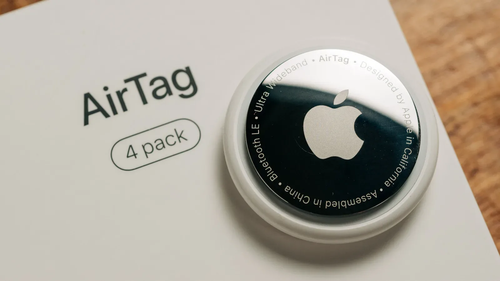 Apple AirTag with its stainless-steel battery cover removed beside a CR2032 coin-cell battery