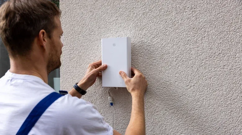 Technician installing a modem on the outside of a house.