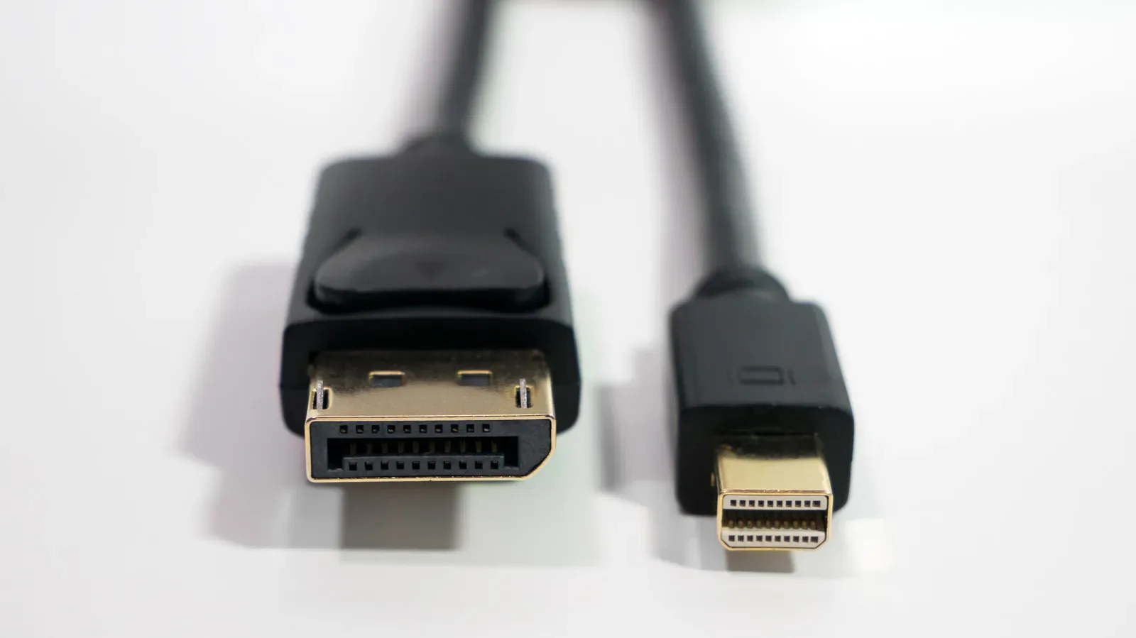 A Mini DisplayPort cable connected to an older laptop beside a modern DisplayPort gaming monitor