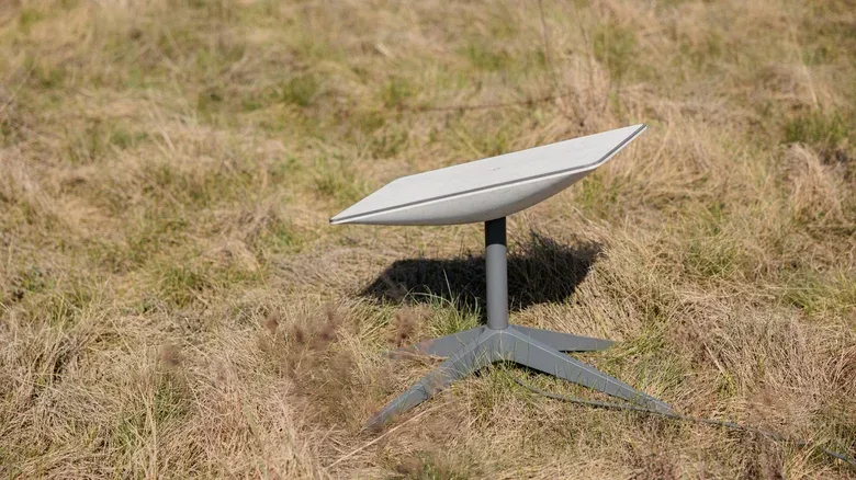 A Starlink dish, placed on grass in a field.