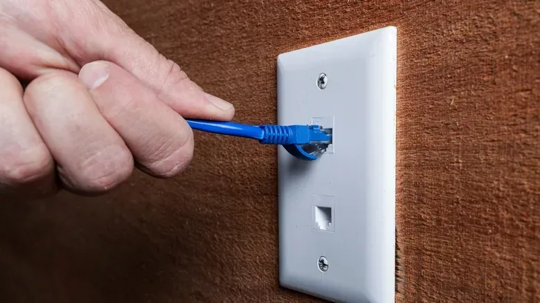 A person's hand connecting an Ethernet cable to a wall plug.