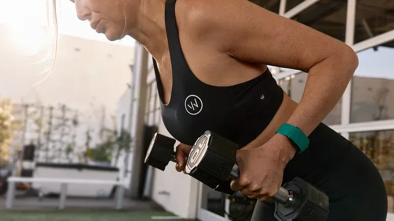 A woman bent over doing rows with weights while wearing a green Whoop tracker.