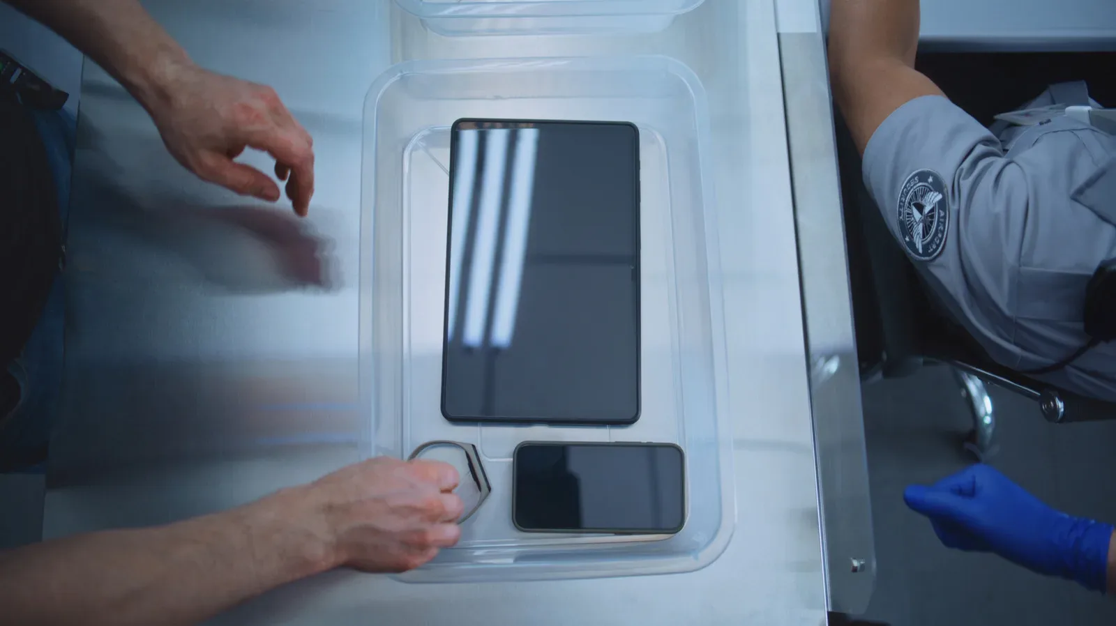 A phone kept inside a carry-on bag beside a handheld gaming console at an airport security checkpoint