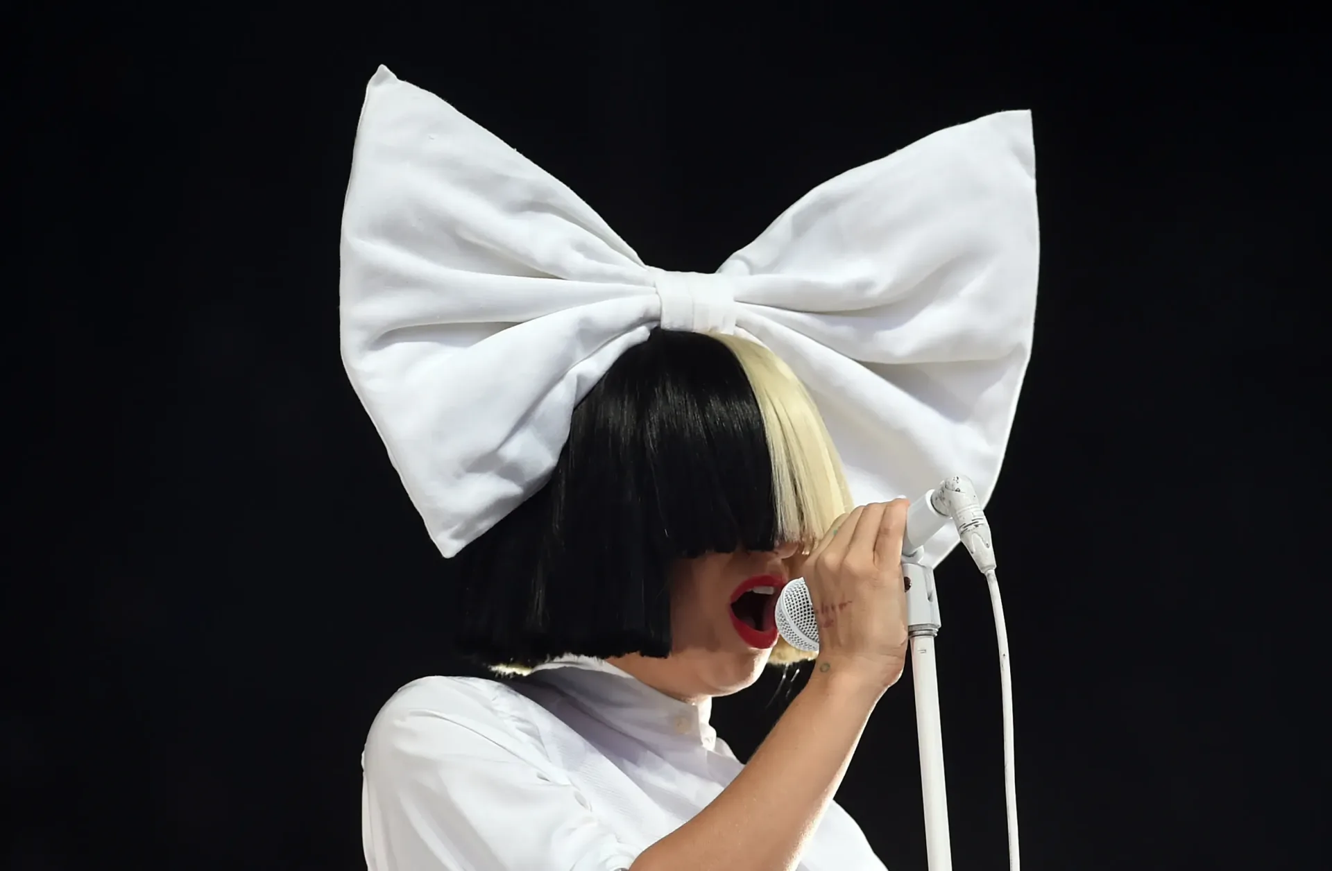 Sia performing onstage under colorful concert lighting