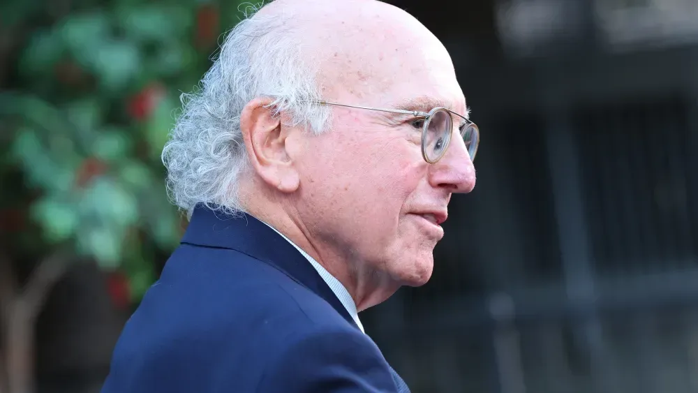 Larry David speaking with collaborators in an archival television image