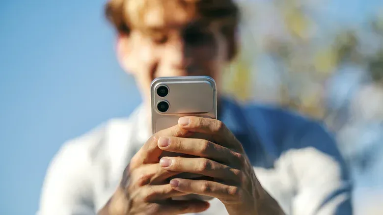 A man out of focus smiles while using his iPhone